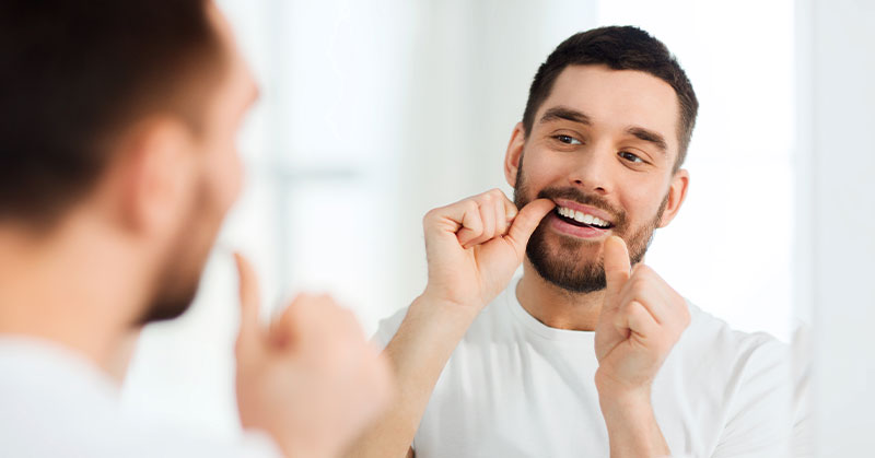 A beard man flossing his teeth Cedar Park Premier Dentistry