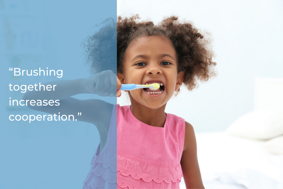 A young girl in a pink dress brushes her teeth with a blue toothbrush. Text on the left reads, "Brushing together increases cooperation—a simple way to support family oral health.
